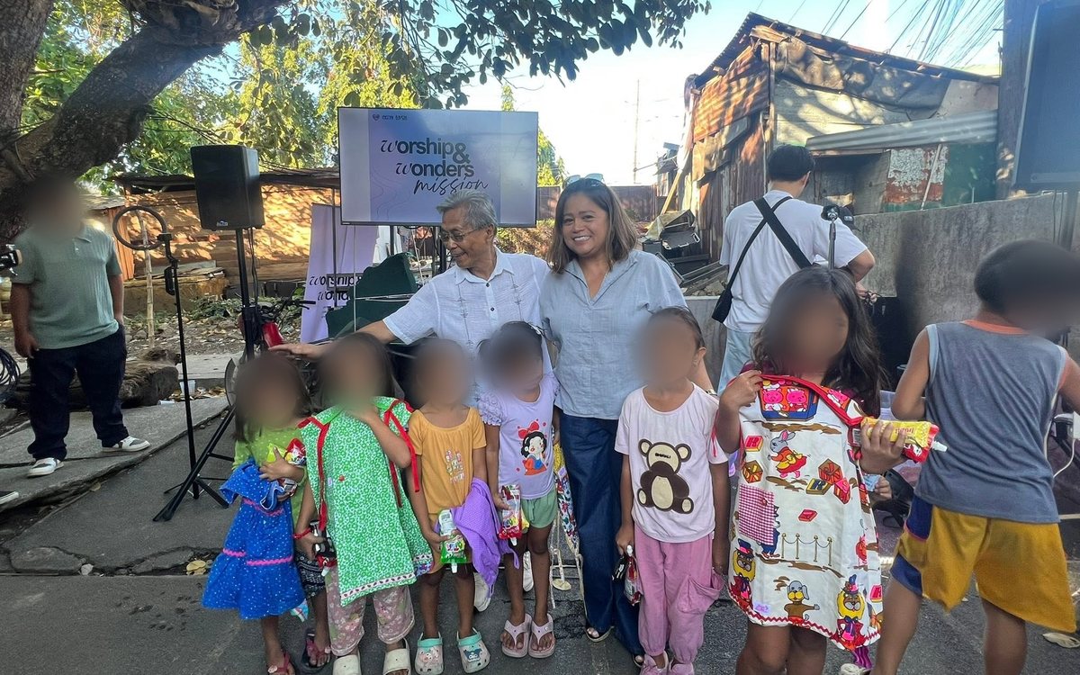 Pastors Ric and Hazel with children holding new dresses and treats at the Worship & Wonders Mission in Biñan, Laguna